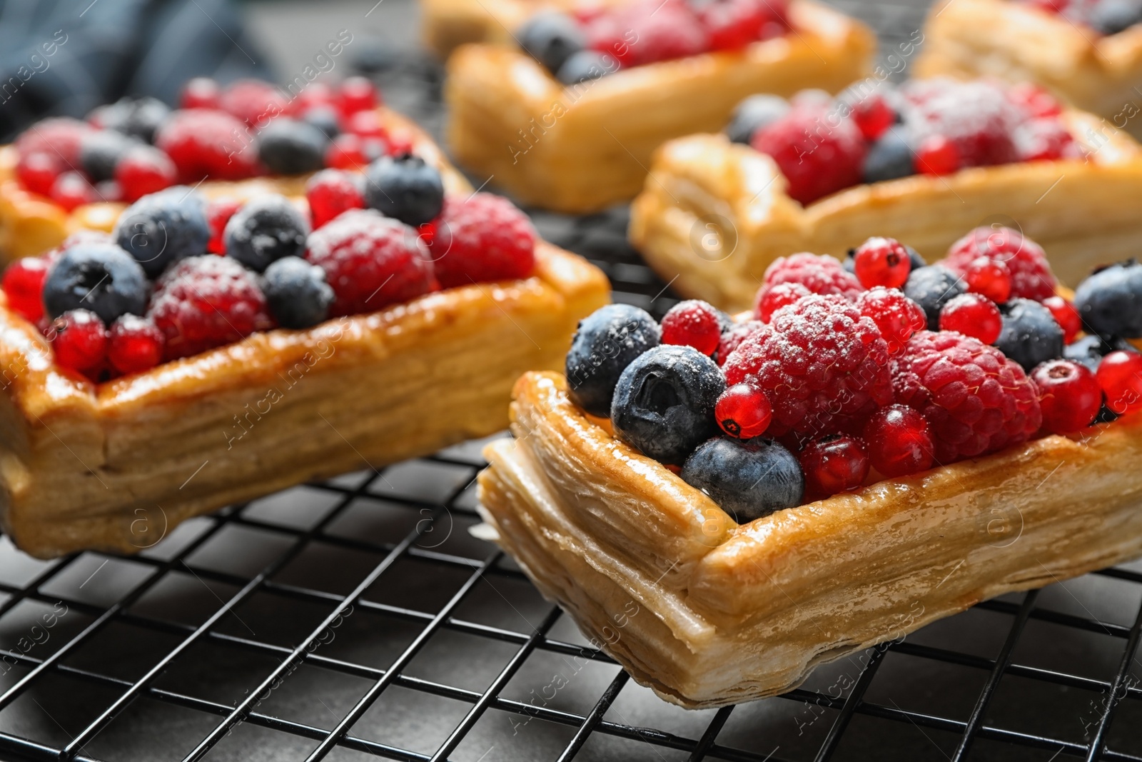 Photo of Cooling rack and fresh delicious puff pastry with sweet berries on grey table, closeup