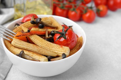 Photo of Tasty roasted baby corn with tomatoes and mushrooms on light grey table, closeup