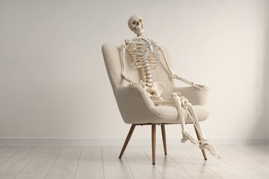 Photo of Waiting concept. Human skeleton sitting in armchair indoors, space for text