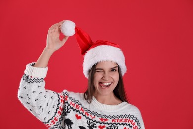 Photo of Playful woman in Santa hat and Christmas sweater on red background