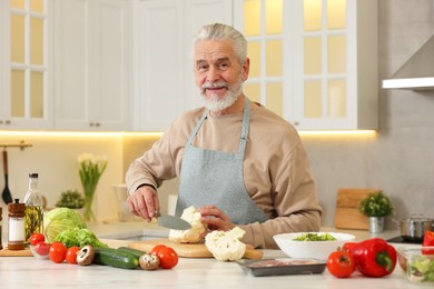 Photo of Happy man cutting cauliflower at table in kitchen