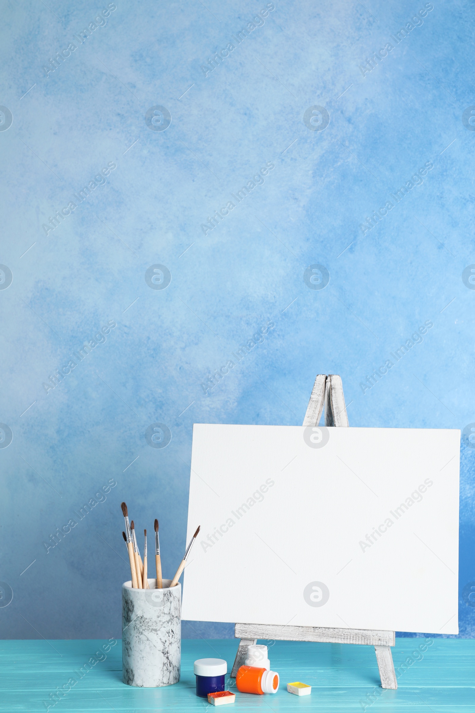 Photo of Wooden easel with blank canvas board and painting tools for children on table near color wall