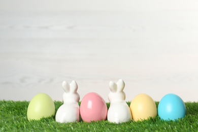 Cute ceramic Easter bunnies and dyed eggs on green grass. Space for text