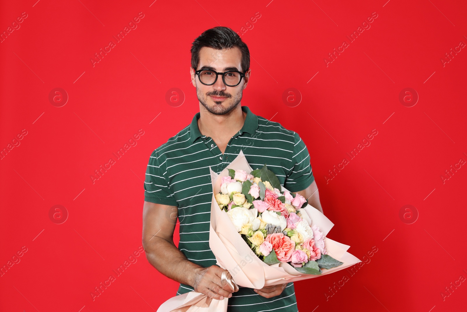 Photo of Young handsome man with beautiful flower bouquet on red background