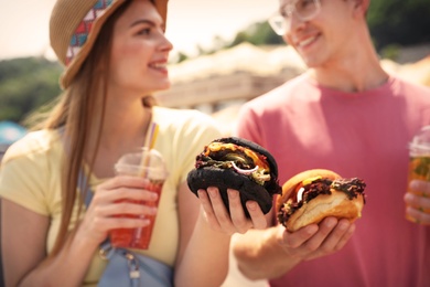Photo of Young happy couple with burgers walking on city street, closeup