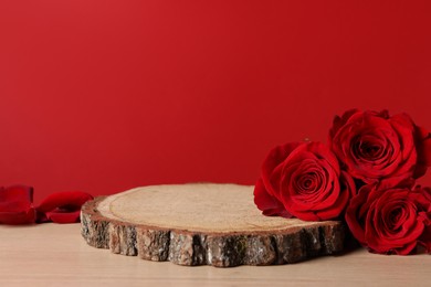 Photo of Presentation for product. Wooden podium and beautiful roses on table against red background, space for text