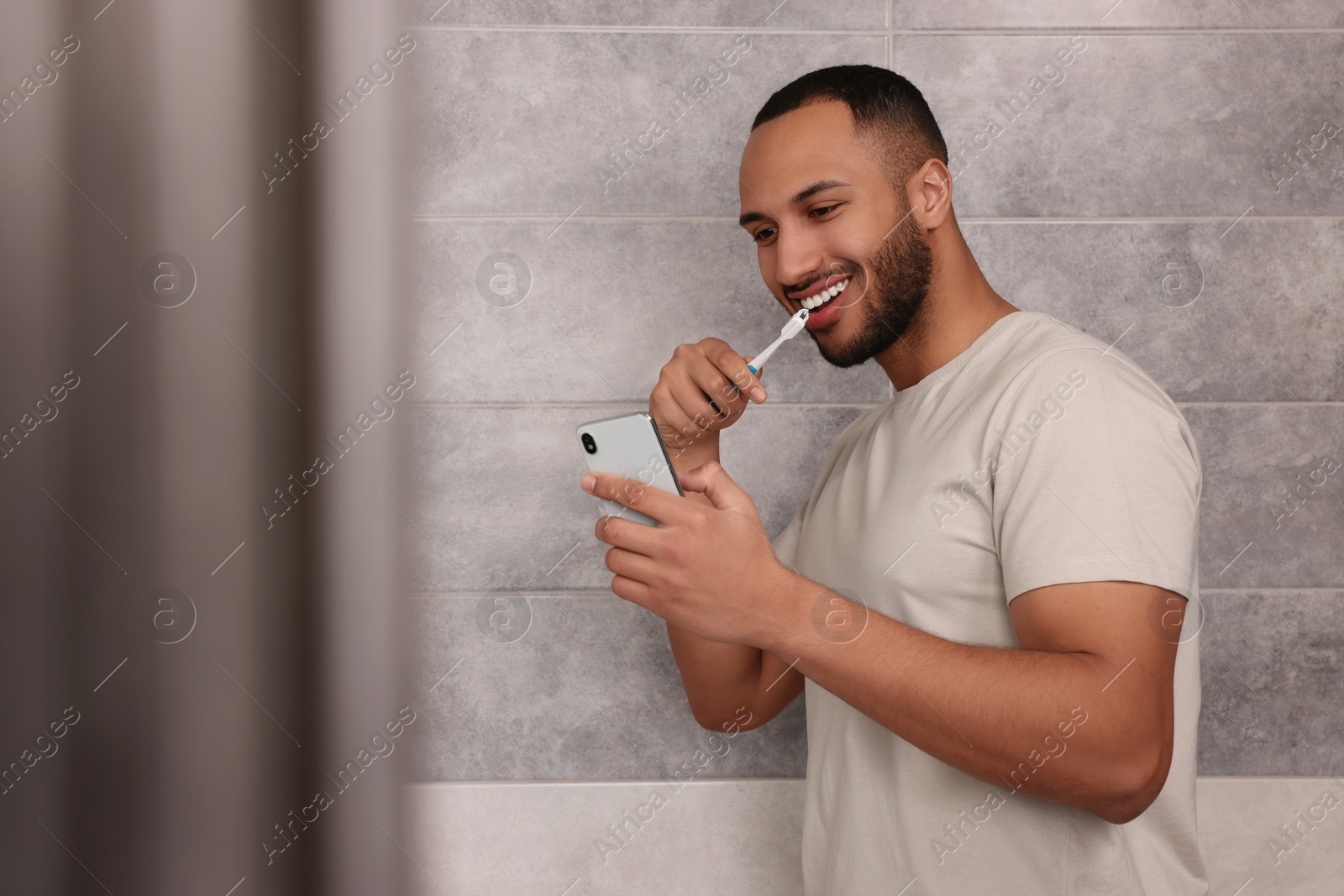 Photo of Happy man using smartphone while brushing teeth in bathroom. Internet addiction