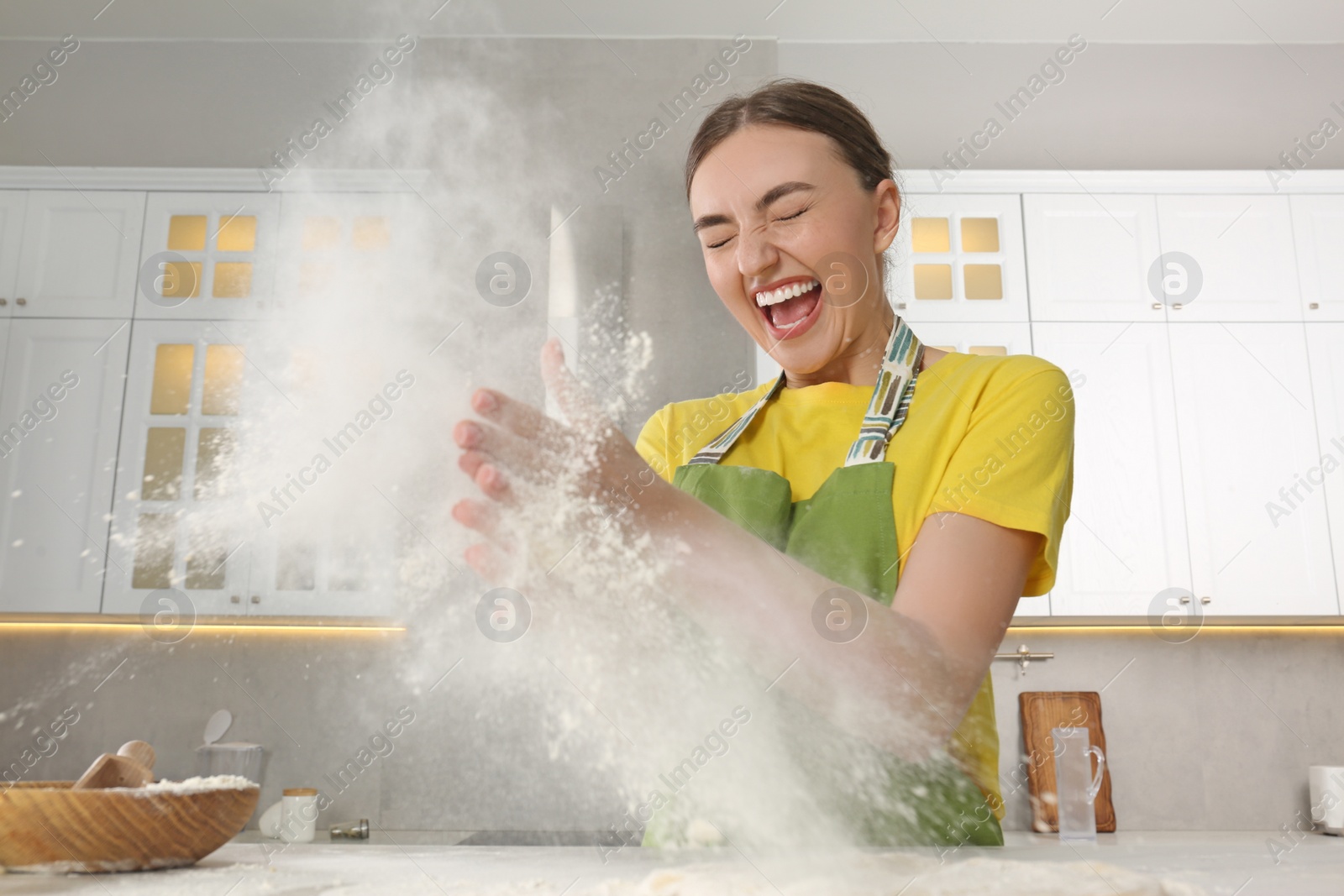 Photo of Funny woman clapping floury hands over messy table in kitchen