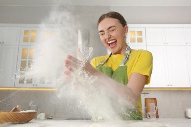 Photo of Funny woman clapping floury hands over messy table in kitchen