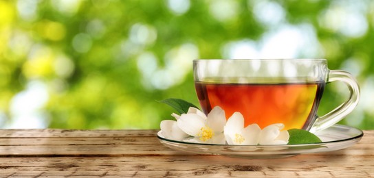 Cup of jasmine tea and fresh flowers on wooden table outdoors, space for text. Banner design