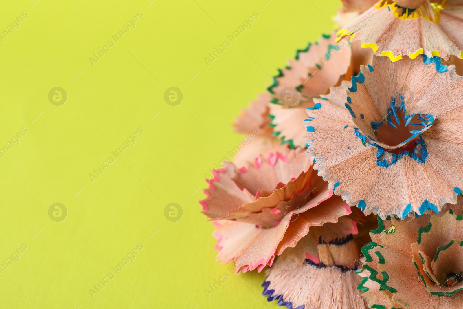 Photo of Pile of colorful pencil shavings on light green background, closeup. Space for text