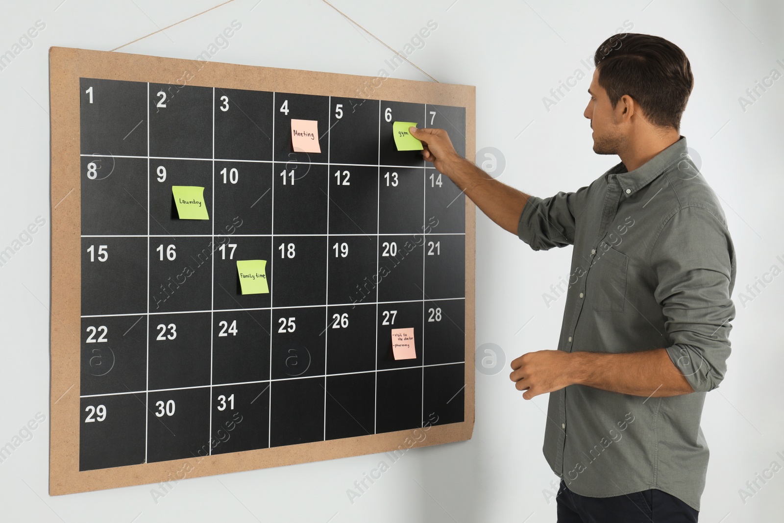 Photo of Handsome man putting sticky note on board calendar