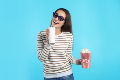 Photo of Woman with 3D glasses, popcorn and beverage during cinema show on color background