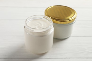 Photo of Jars with delicious organic yogurt on white wooden table, closeup