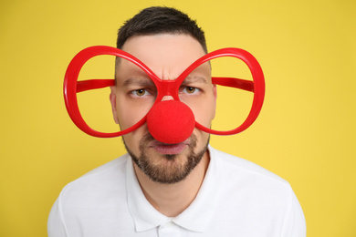 Photo of Man with clown nose and funny glasses on yellow background. April fool's day