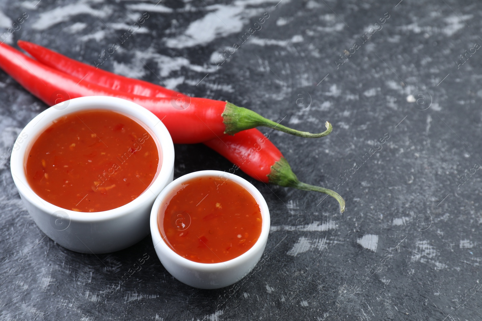 Photo of Spicy chili sauce and peppers on black textured table, space for text