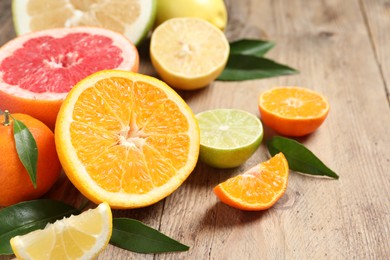 Different ripe citrus fruits with green leaves on wooden table, closeup