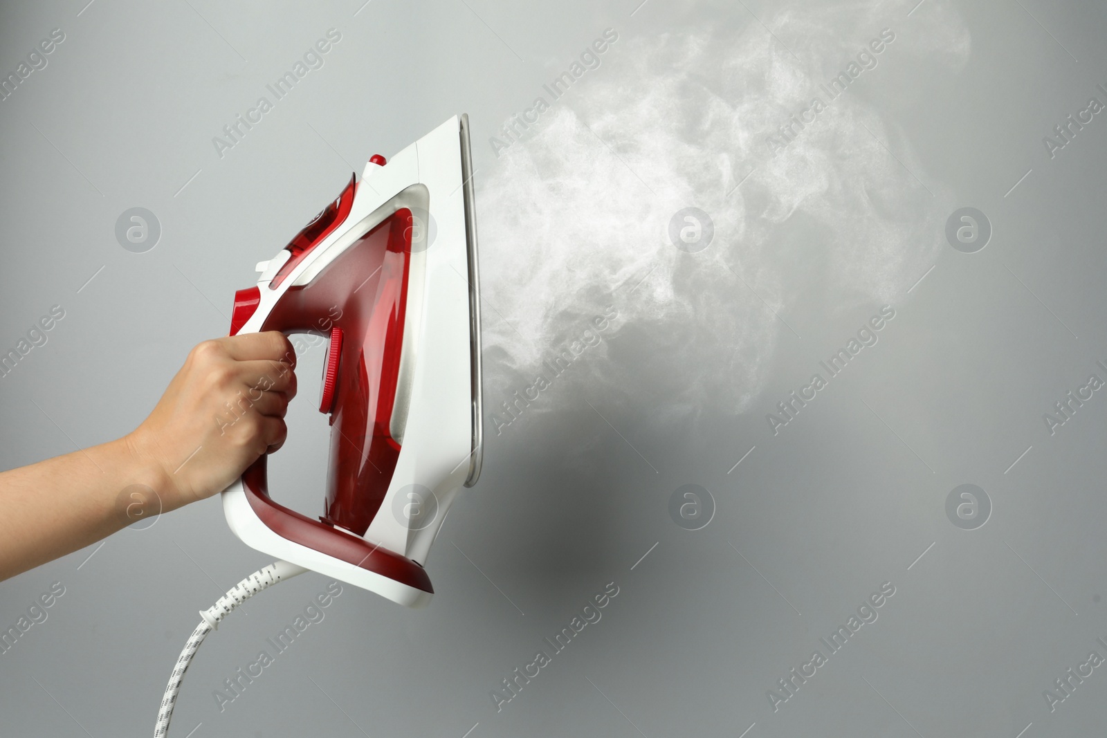 Image of Woman holding modern iron with steam on light grey background, closeup. Space for text