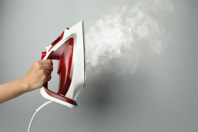 Woman holding modern iron with steam on light grey background, closeup. Space for text