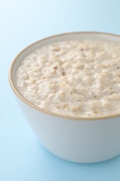 Photo of Tasty boiled oatmeal in bowl on light blue table, closeup