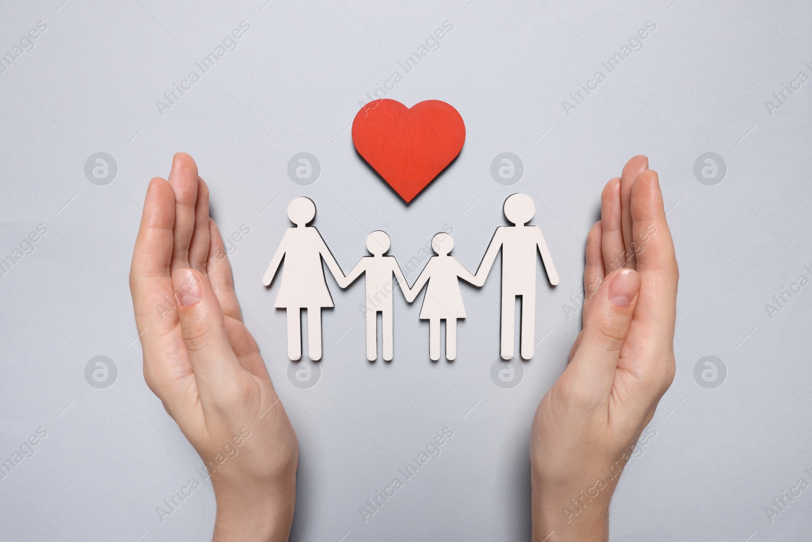 Photo of Woman protecting figures of family and heart on light background, top view. Insurance concept