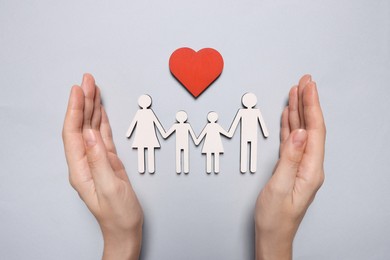 Photo of Woman protecting figures of family and heart on light background, top view. Insurance concept