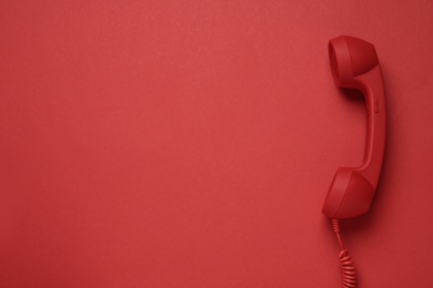 Corded telephone handset on red background, top view. Hotline concept
