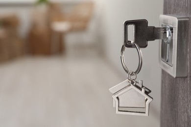 Photo of Mortgage and real estate. Open door with key and house shaped keychain against blurred background, space for text