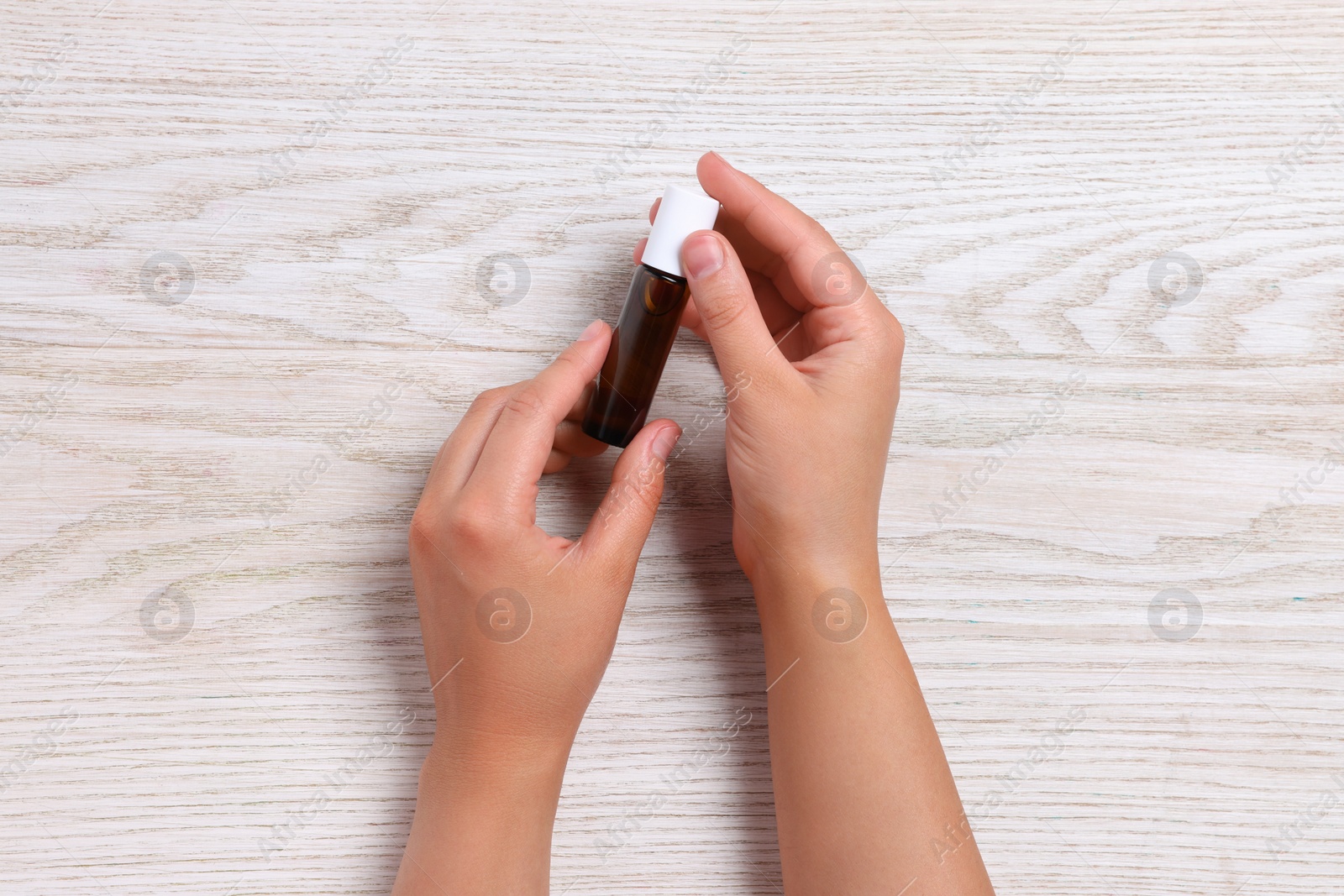 Photo of Woman with bottle of essential oil on wooden background, top view