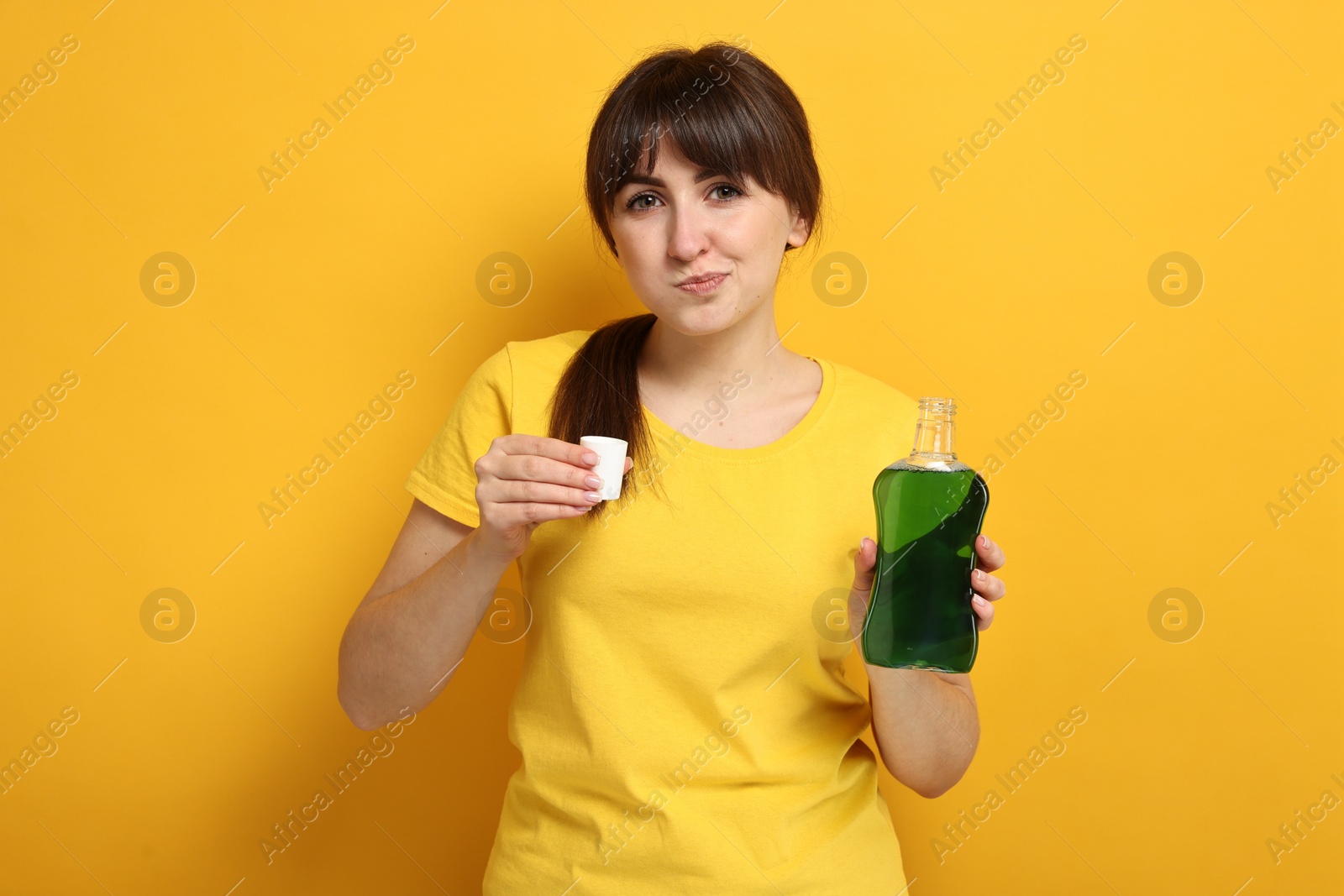 Photo of Young woman using mouthwash on yellow background