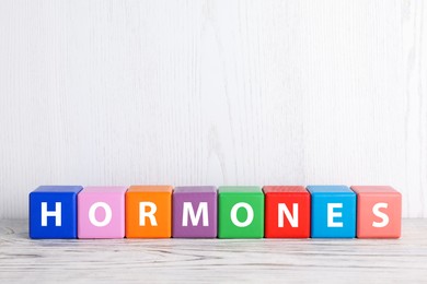 Photo of Word HORMONES made with colorful cubes on white wooden table