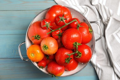 Photo of Many different ripe tomatoes in colander on light blue wooden table, top view