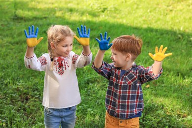 Photo of Little girl and boy with hands painted in Ukrainian flag colors outdoors. Love Ukraine concept