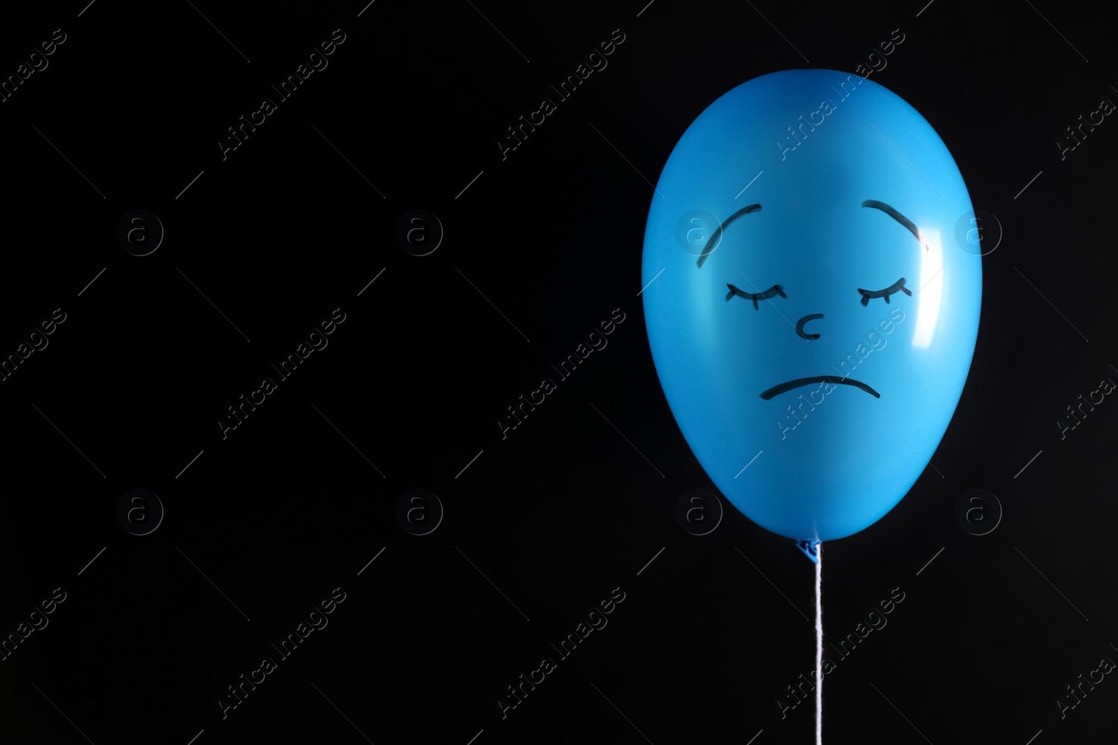 Photo of Air balloon with drawn sad face on black background. Space for text