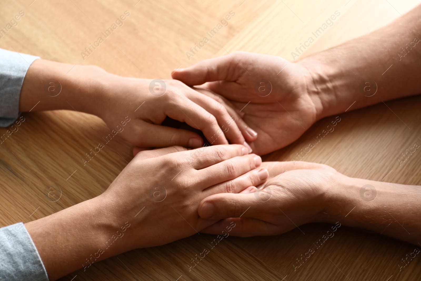 Photo of Young people holding hands on wooden background, closeup. Happy family