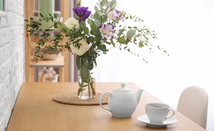 Photo of Teapot, cup and flowers on wooden dining table indoors. Kitchen interior
