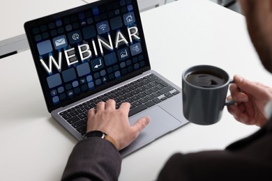 Online webinar, web page on computer screen. Man with cup of coffee using laptop at white table, closeup