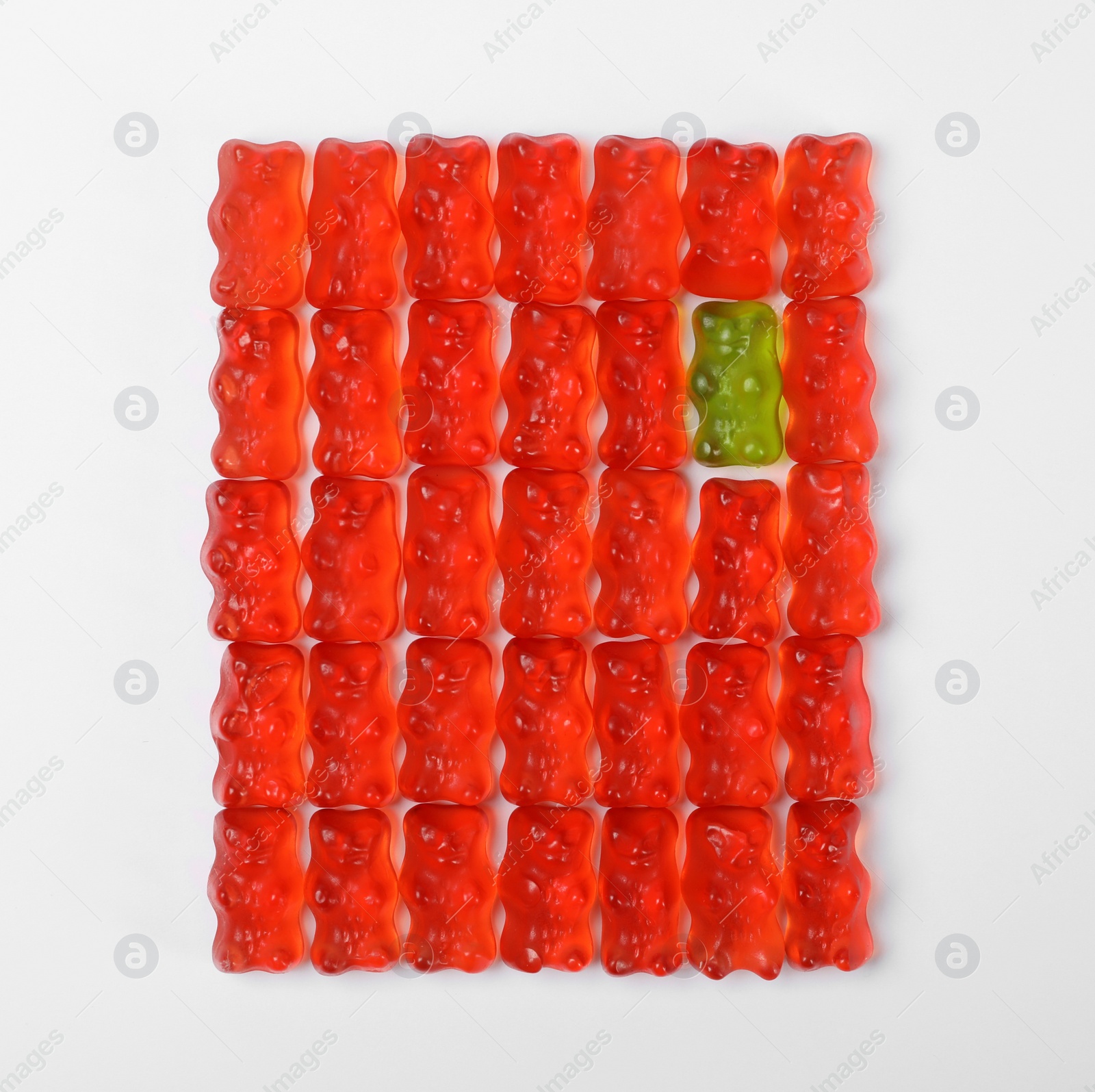 Photo of Green jelly bear among red ones on white background, top view. Individuality concept