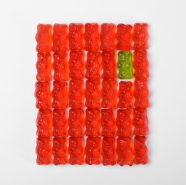 Green jelly bear among red ones on white background, top view. Individuality concept