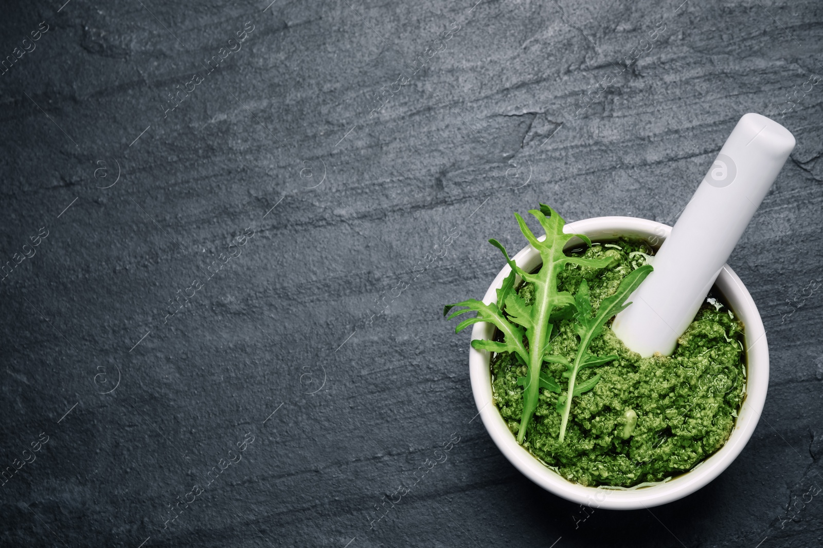 Photo of Mortar with tasty arugula pesto on black table, top view. Space for text