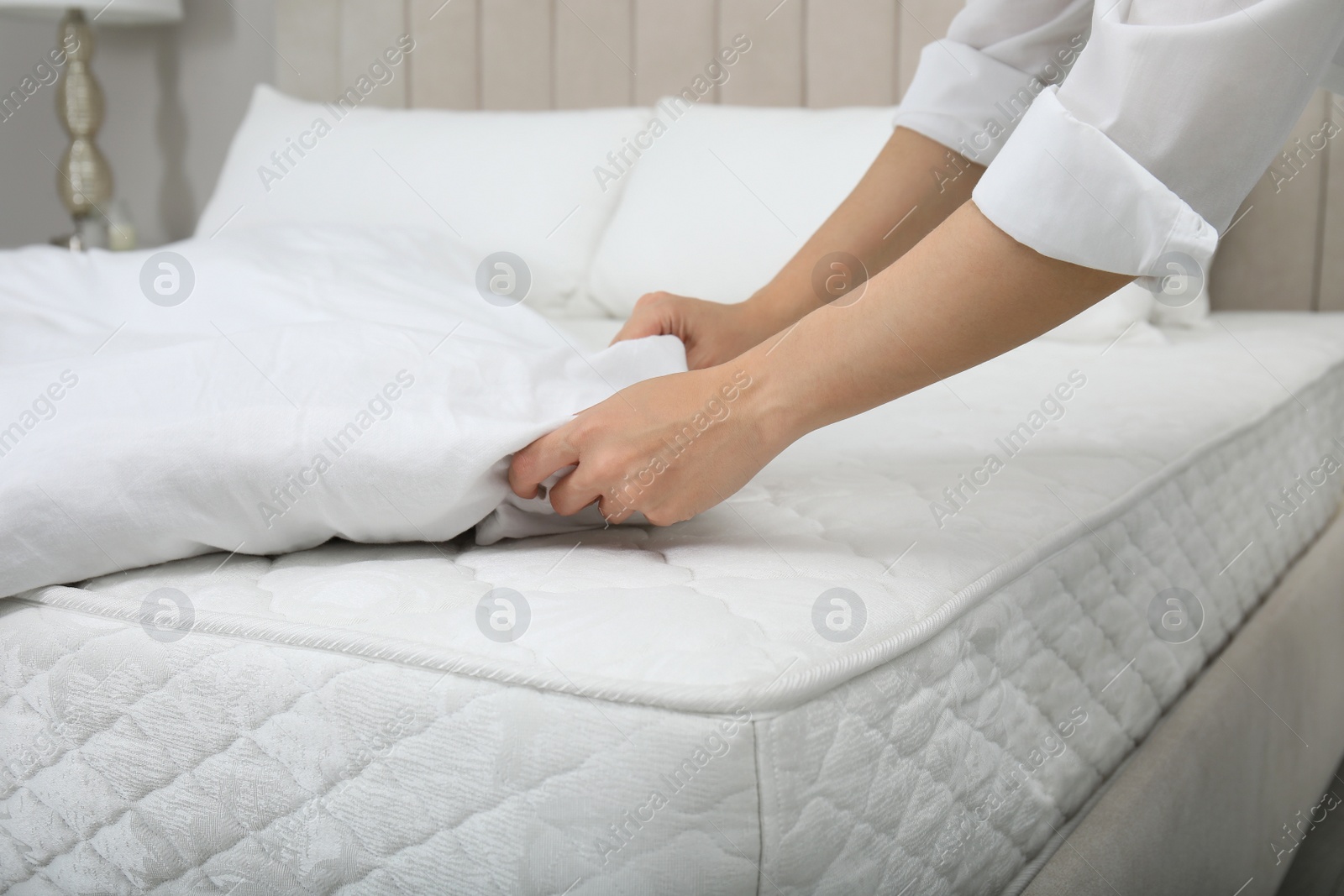 Photo of Woman putting blanket over soft white mattress on bed indoors, closeup