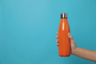 Photo of Woman holding modern orange thermos on light blue background, closeup. Space for text