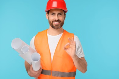 Photo of Architect in hard hat with drafts showing OK gesture on light blue background