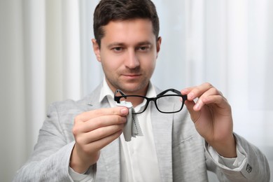 Photo of Man wiping glasses with microfiber cloth indoors, selective focus