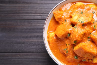 Photo of Bowl of delicious chicken curry on black wooden table, top view. Space for text