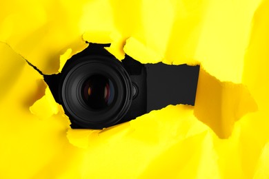 Photo of Hidden camera spying through torn hole in yellow paper, space for text