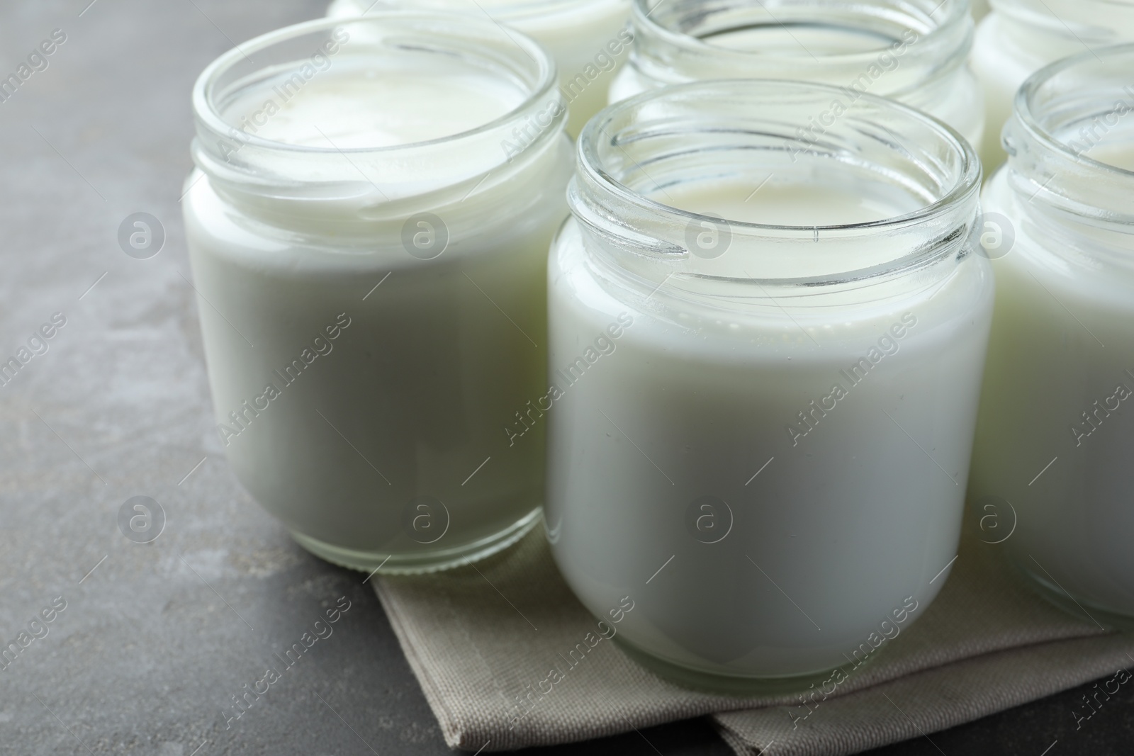 Photo of Tasty yogurt in glass jars on grey table, closeup