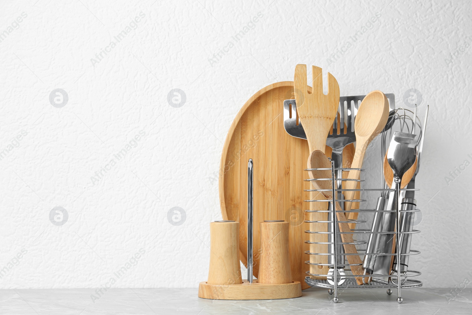 Photo of Set of kitchen utensils in stand on stone table near light wall. Space for text