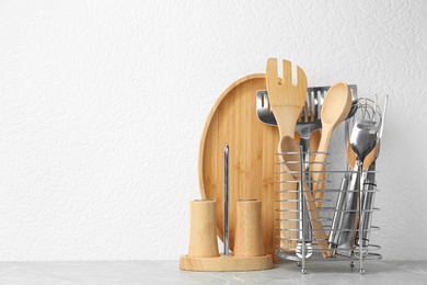 Photo of Set of kitchen utensils in stand on stone table near light wall. Space for text