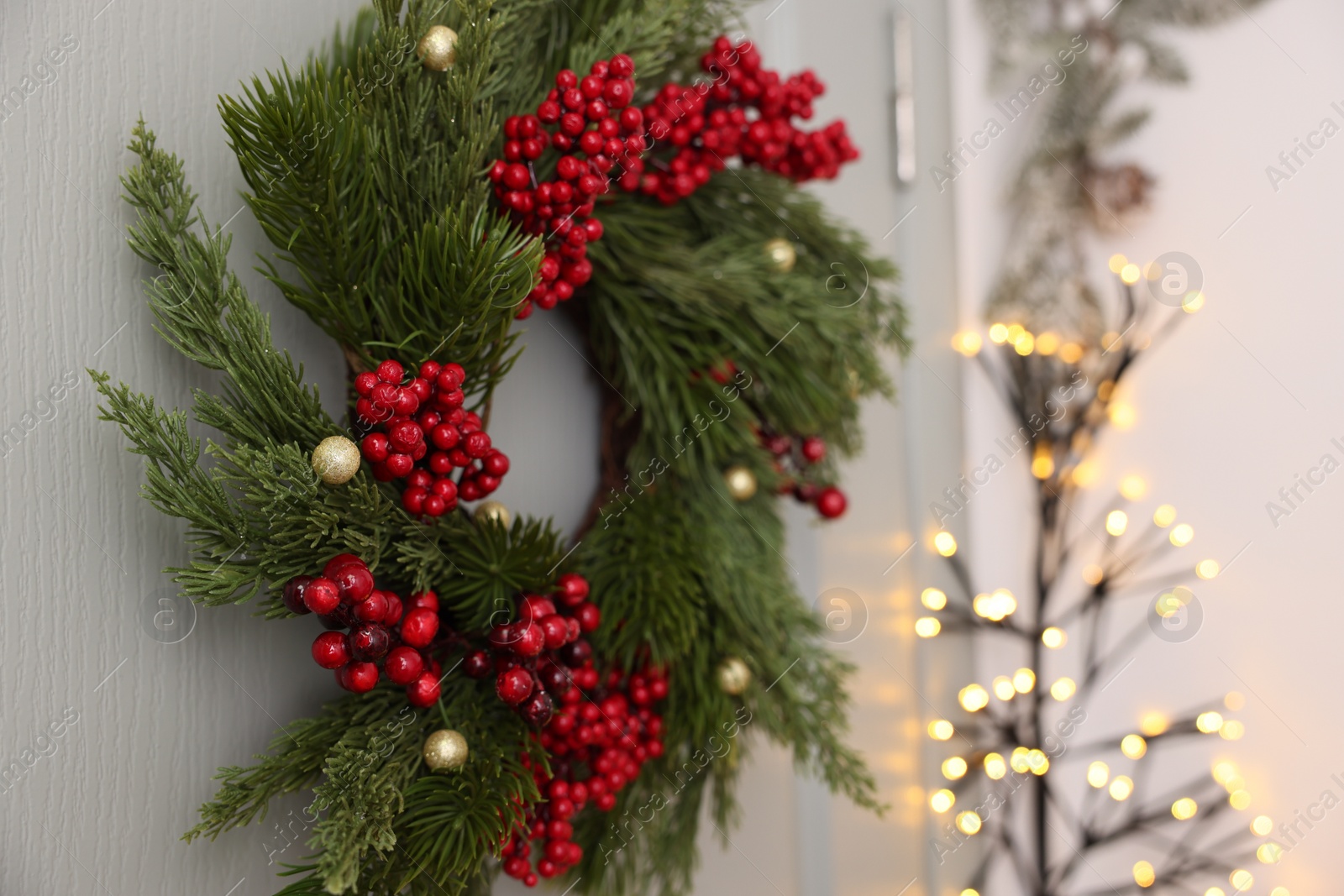 Photo of Beautiful Christmas wreath with red berries and decor hanging on white door, closeup. Space for text